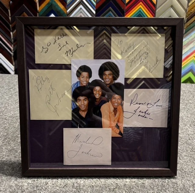 Framed collage featuring a color photograph of five young African American friends smiling, surrounded by six handwritten notes and signatures, with a background of colorful framing supplies.