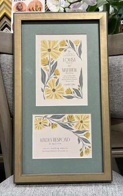 A framed wedding invitation and response card with yellow flowers and gray leaves, set against a teal background. The invitation is for Louisa and Matthew's wedding on May 7, 2023, and the response card requests responses by April 15.