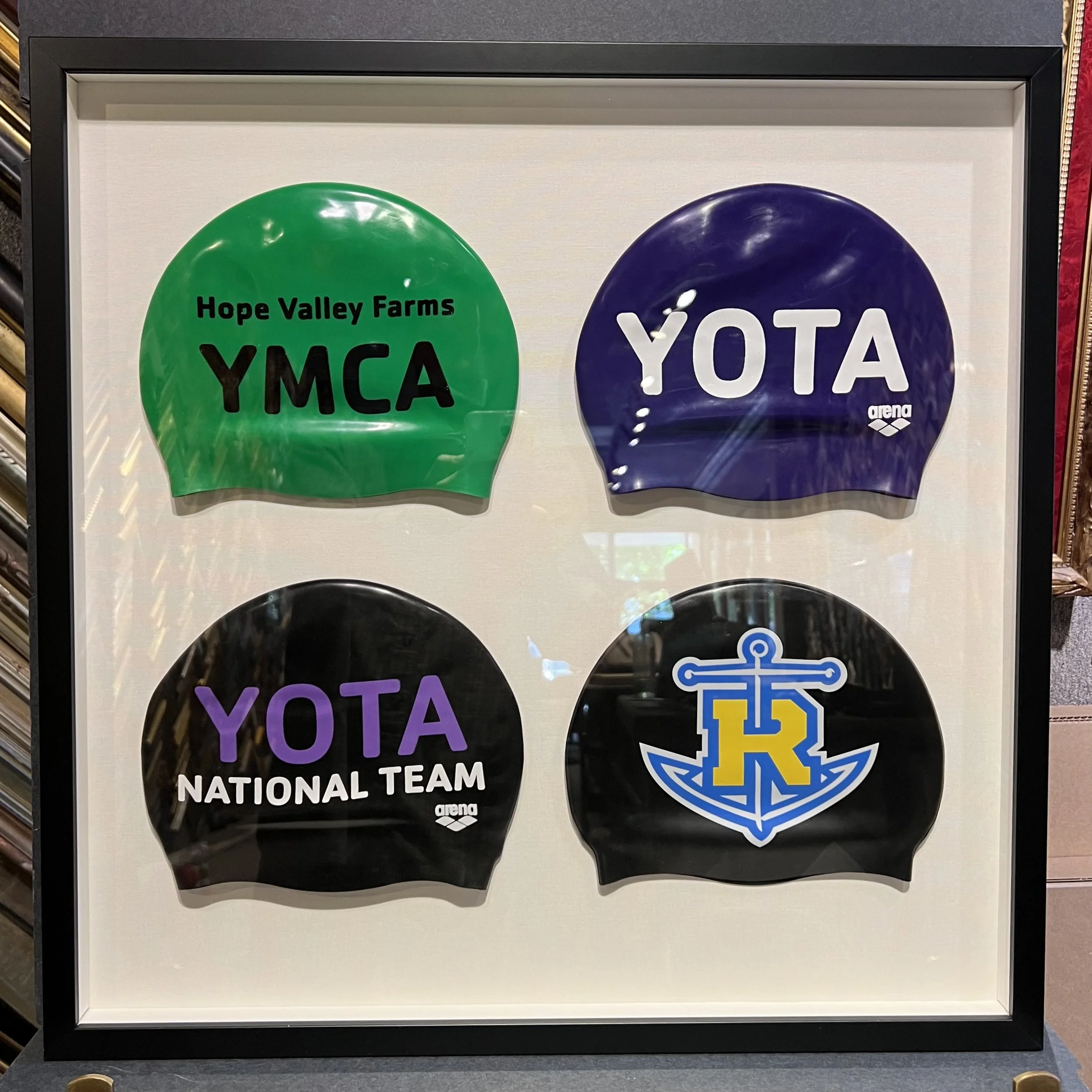 Framed collage featuring two swimming caps: one green with black text saying "Hope Valley Farms YMCA" and one blue with white text saying "YOTA" and a yellow and blue logo.