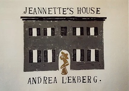 A sign with the text 'Jeannette's House' and 'Andrea Lekberg.' It features an illustration of a house with multiple windows and a small figure of a woman outside.