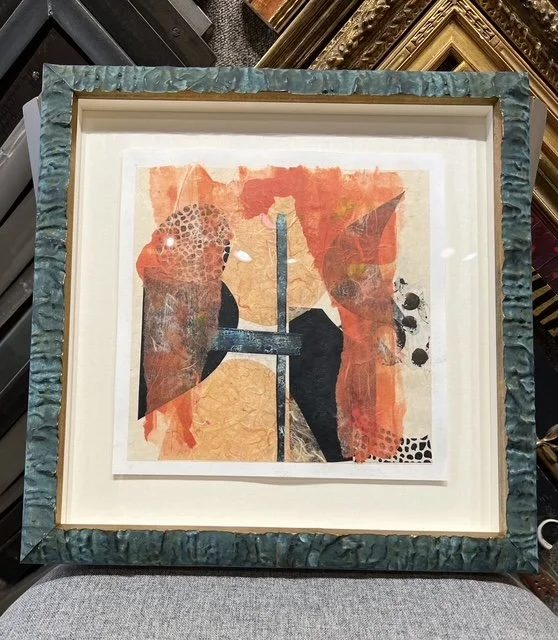 Abstract artwork with orange, black, and beige shapes framed in a decorative blue-green frame.