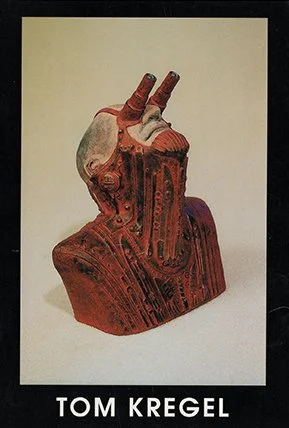 A sculpture of a hand making a peace sign, mounted on a wooden base, with the artist's name Tom Kregel written below.