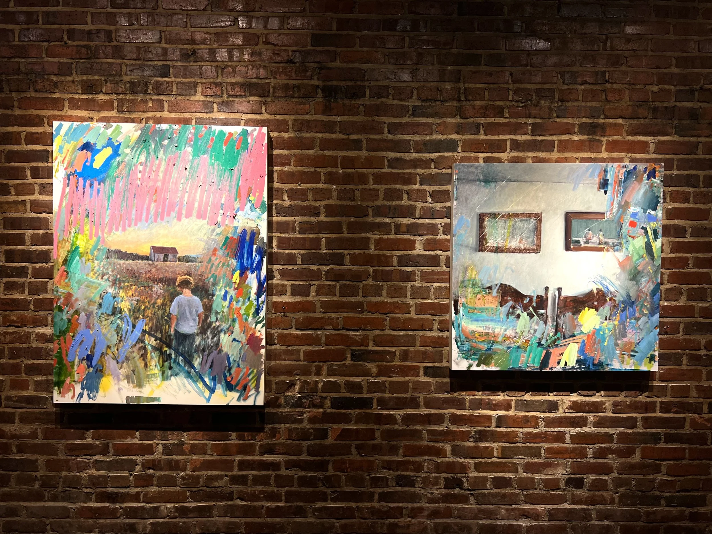Two colorful abstract paintings on display against a brick wall.