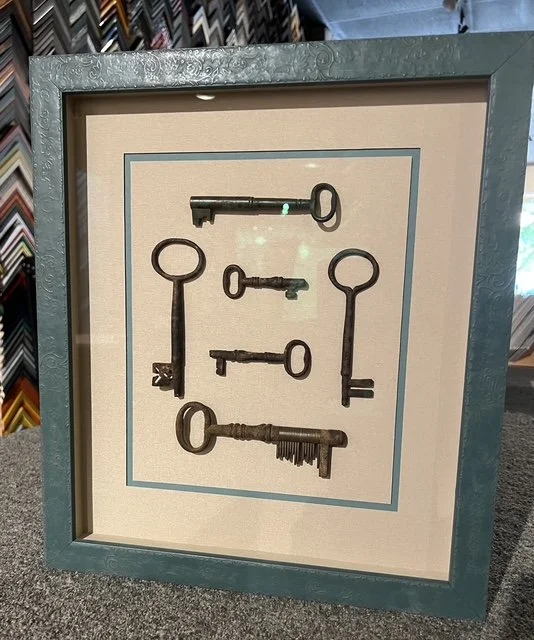 A framed display of six vintage keys arranged in two rows inside a shadow box with a blue border.