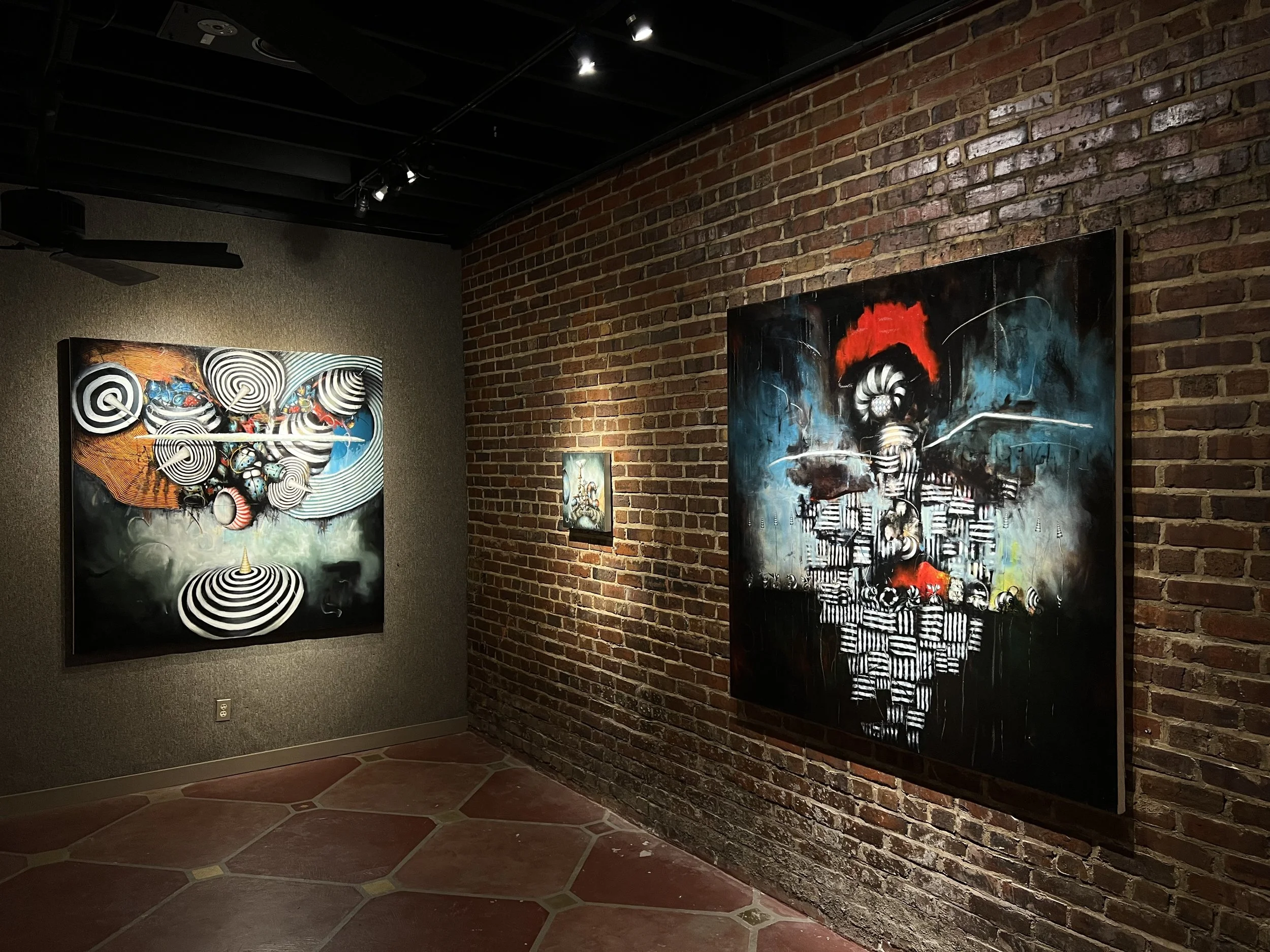Art gallery with colorful abstract paintings on a brick wall.