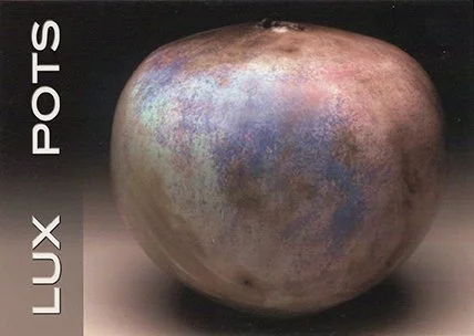 Close-up of a metallic object with a bluish iridescent surface, labeled 'Lux Pots' along the side.