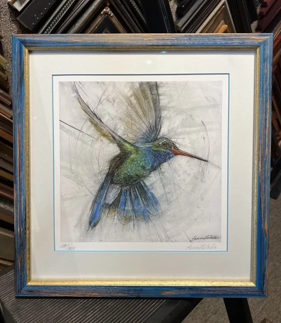 Framed artwork of a hummingbird with outstretched wings, painted in soft, realistic colors.