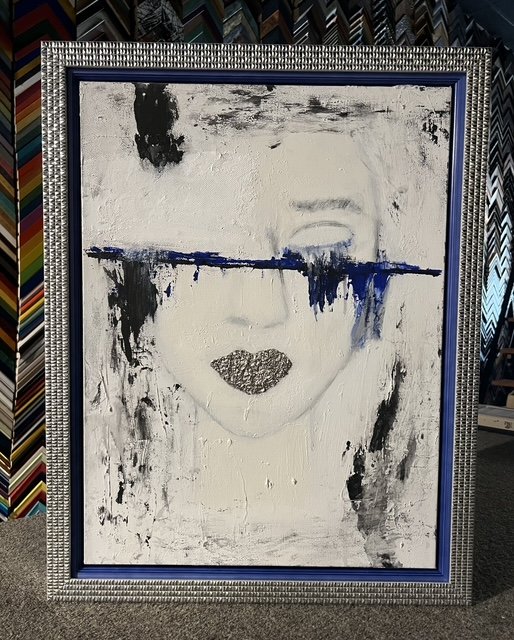 Abstract portrait of a woman's face with only lips and part of the nose visible, with a horizontal blue line across where the eyes would be, in a decorative silver frame.