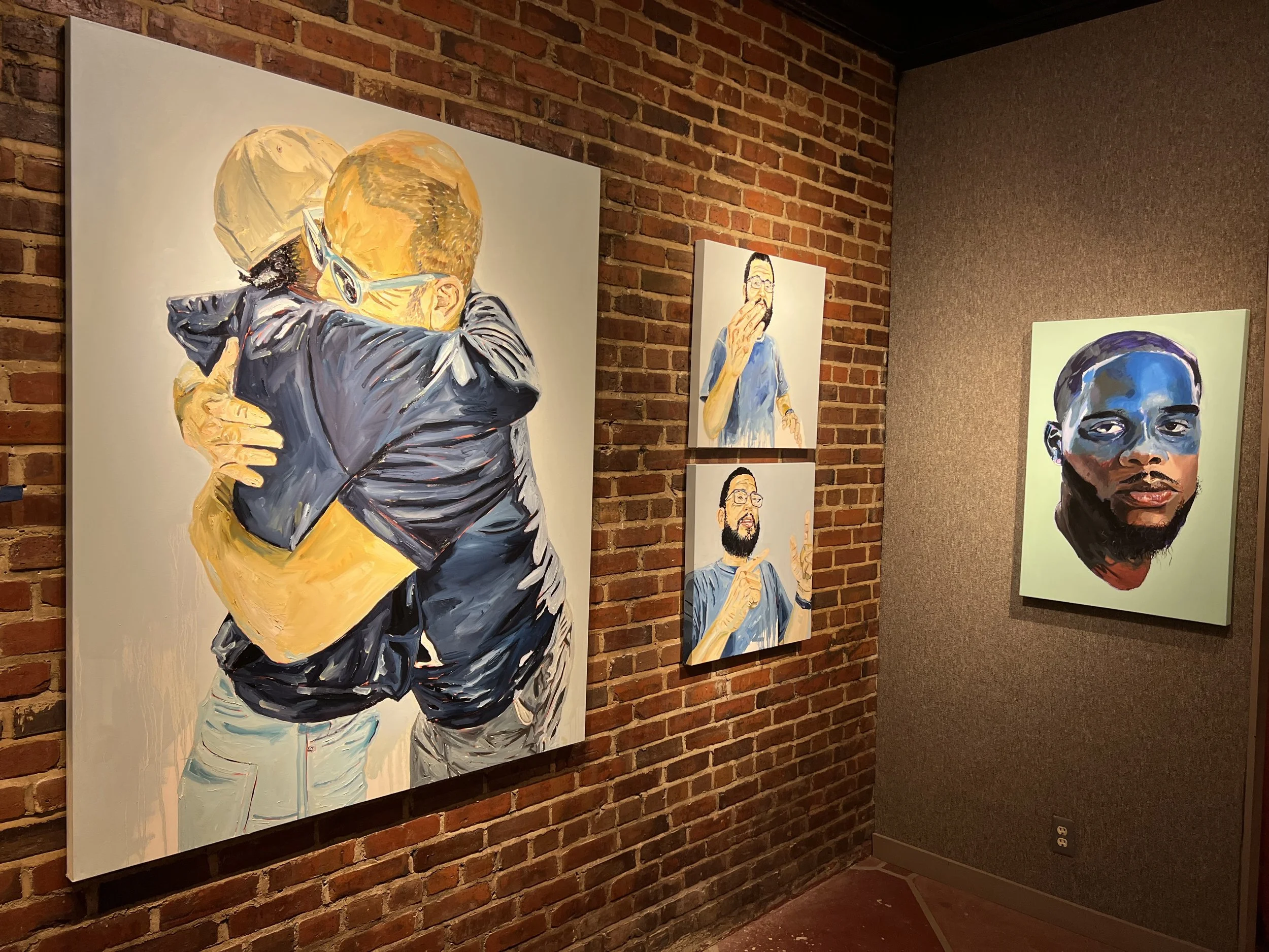 Portrait paintings displayed on a brick wall in an art gallery.