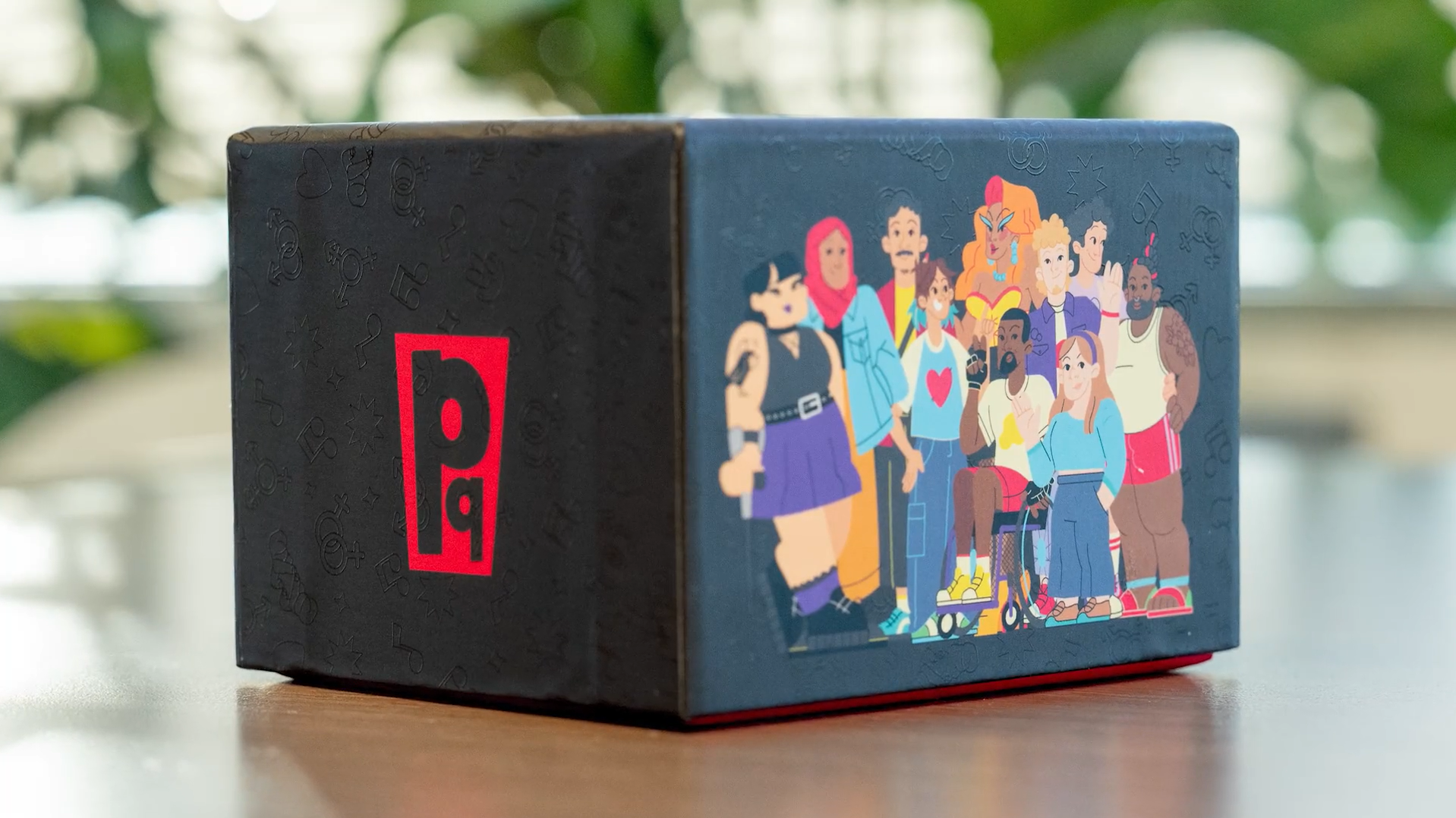 A cardboard box with a colorful illustration of diverse animated characters, including a woman with a mohawk, a person in a wheelchair, and others with various styles, standing together.