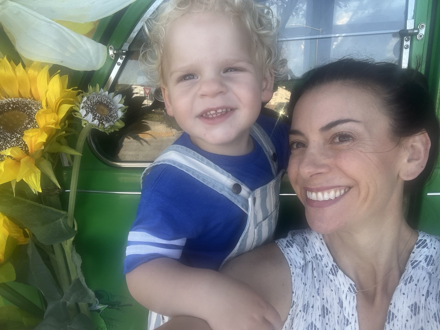 A woman and a young boy smiling for a selfie inside a green-painted vehicle with flowers on the side.