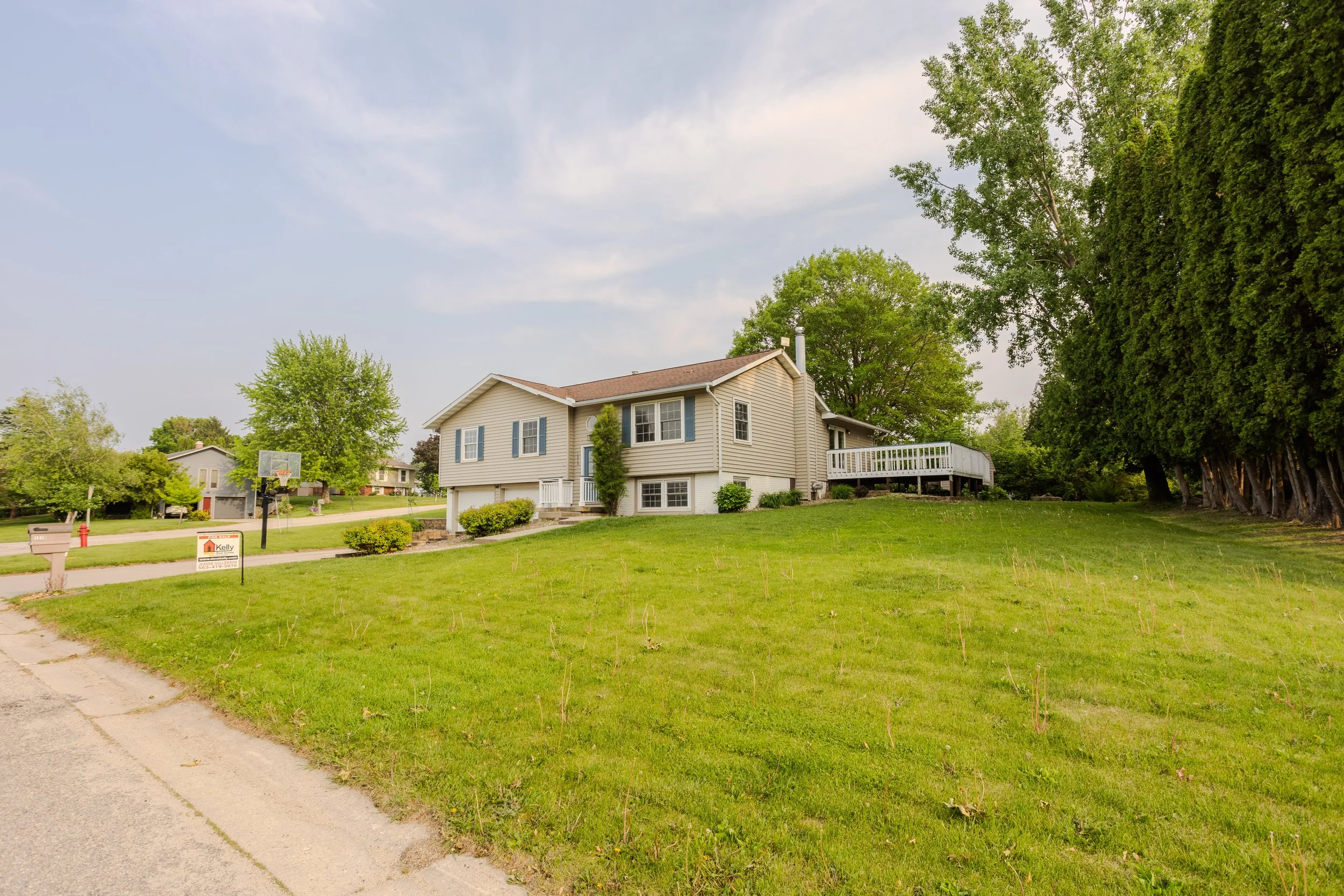 A suburban residential neighborhood with a house, green lawn, trees, and a clear sky.