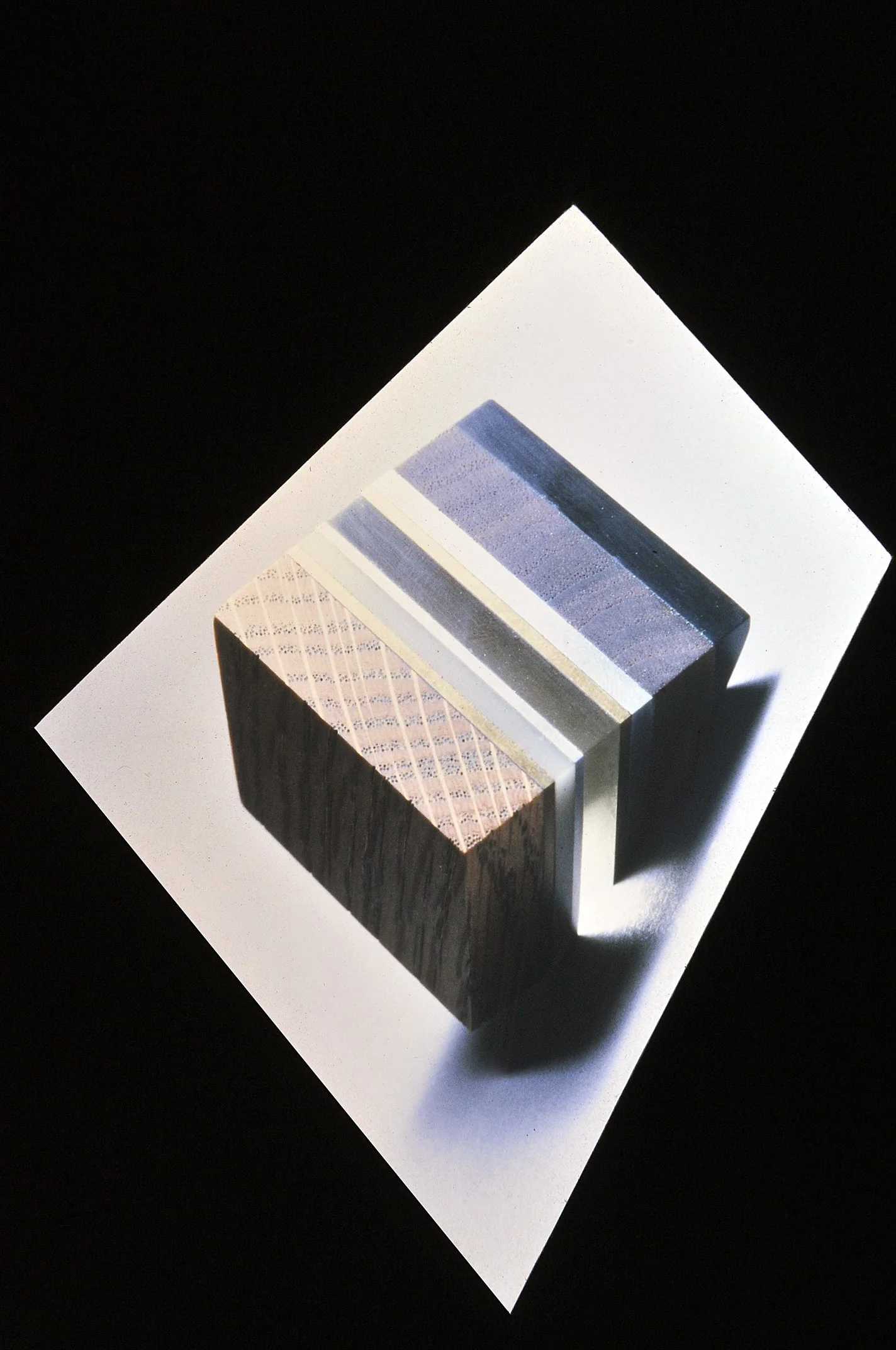 Colorful striped pattern on a rectangular block with a black and white textured side, placed on a white surface against a black background.