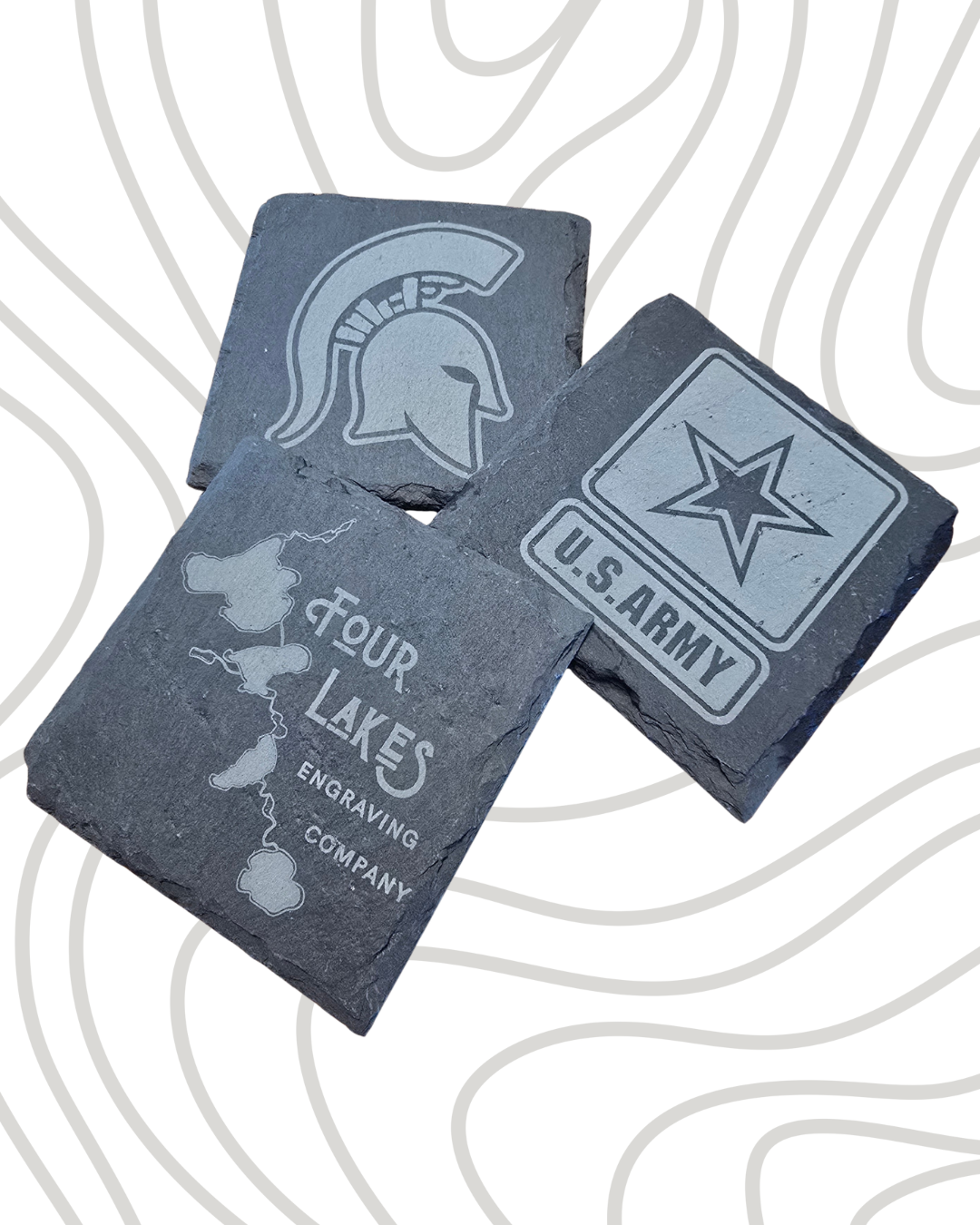 Three engraved slate coasters with military and regional logos on a patterned background.