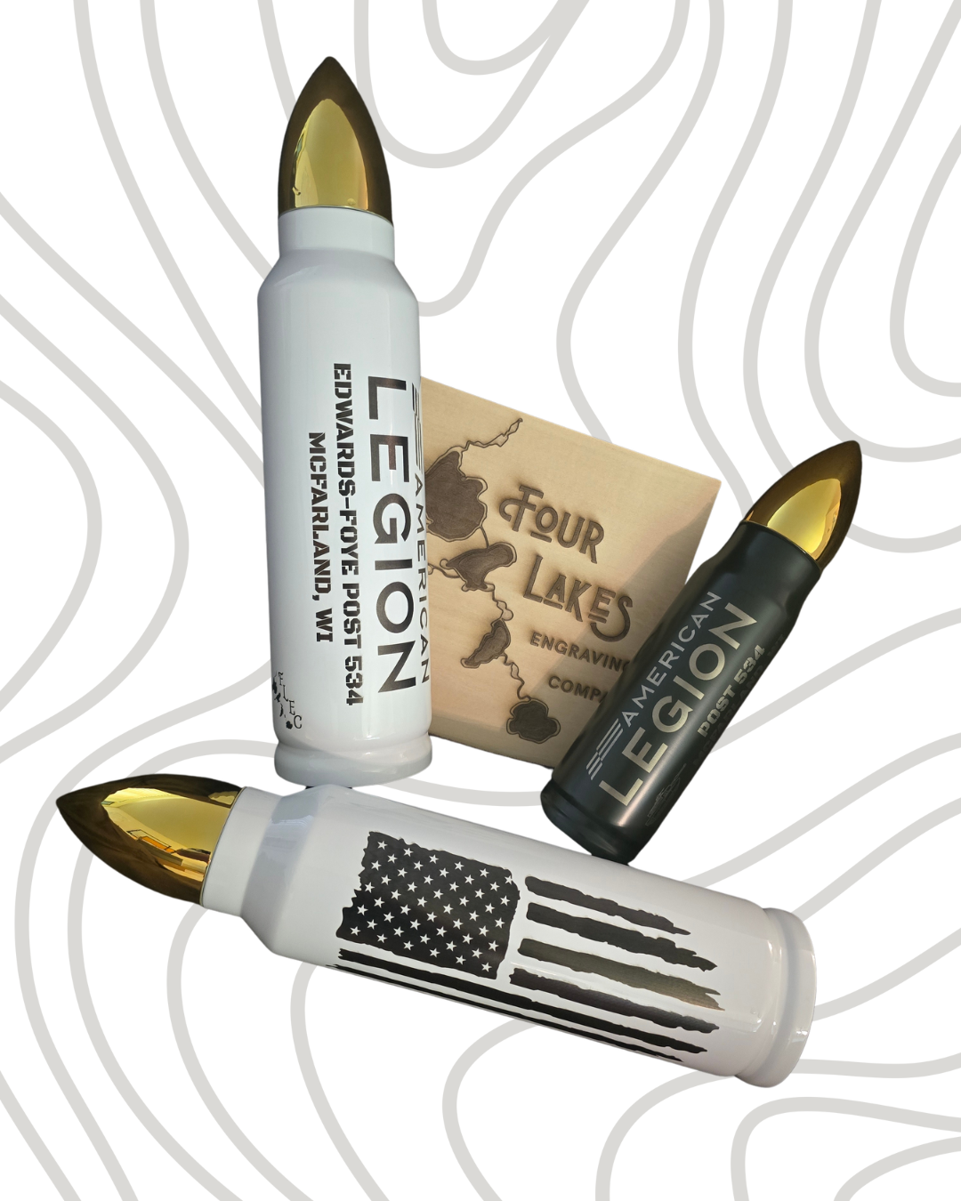 Three bullet-shaped containers with laser-engraved designs, positioned around a small wooden box with engraved text and a map, set against a patterned background.