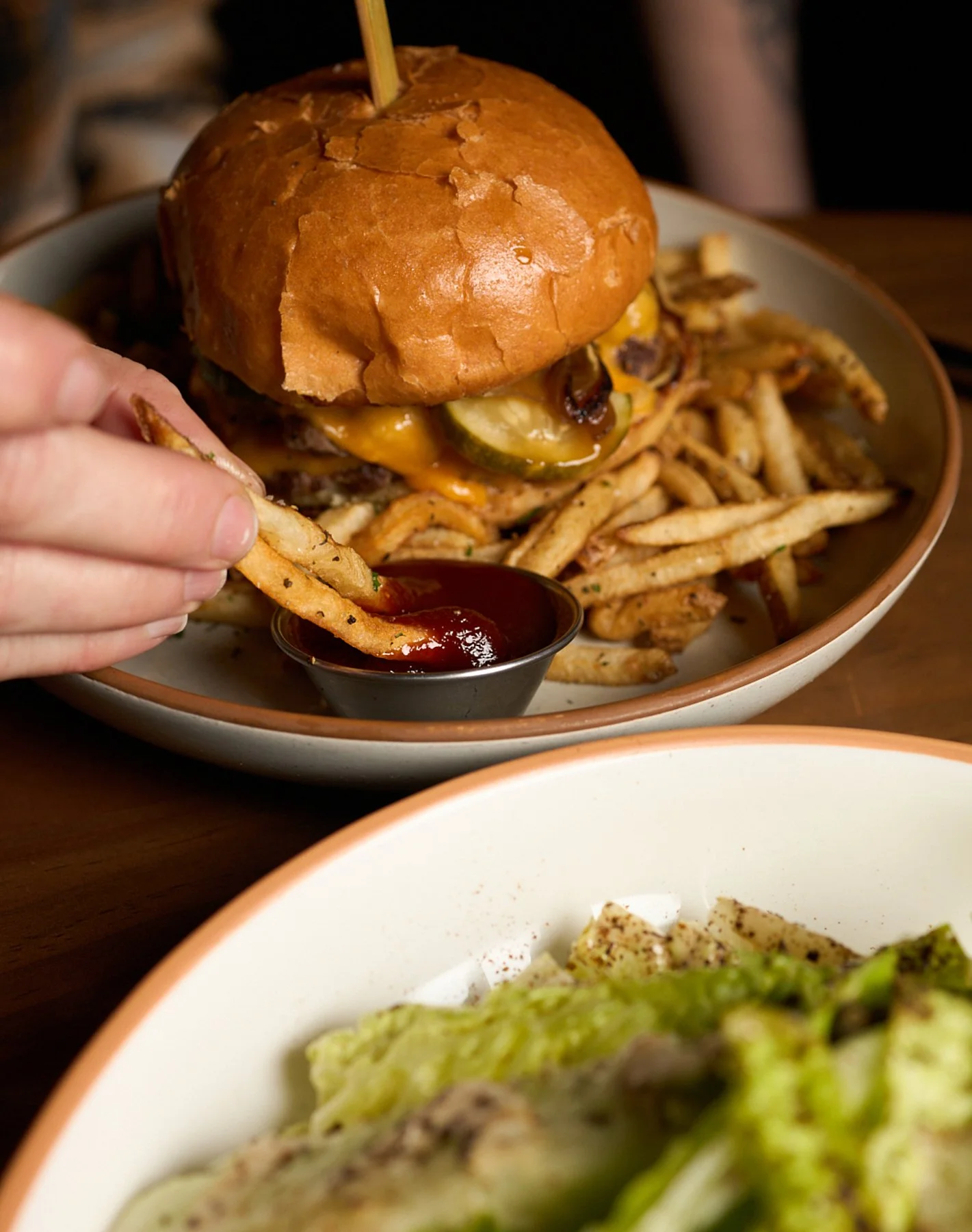 Close-up of a burger with fries, pickles, and melted cheese, served with ketchup.
