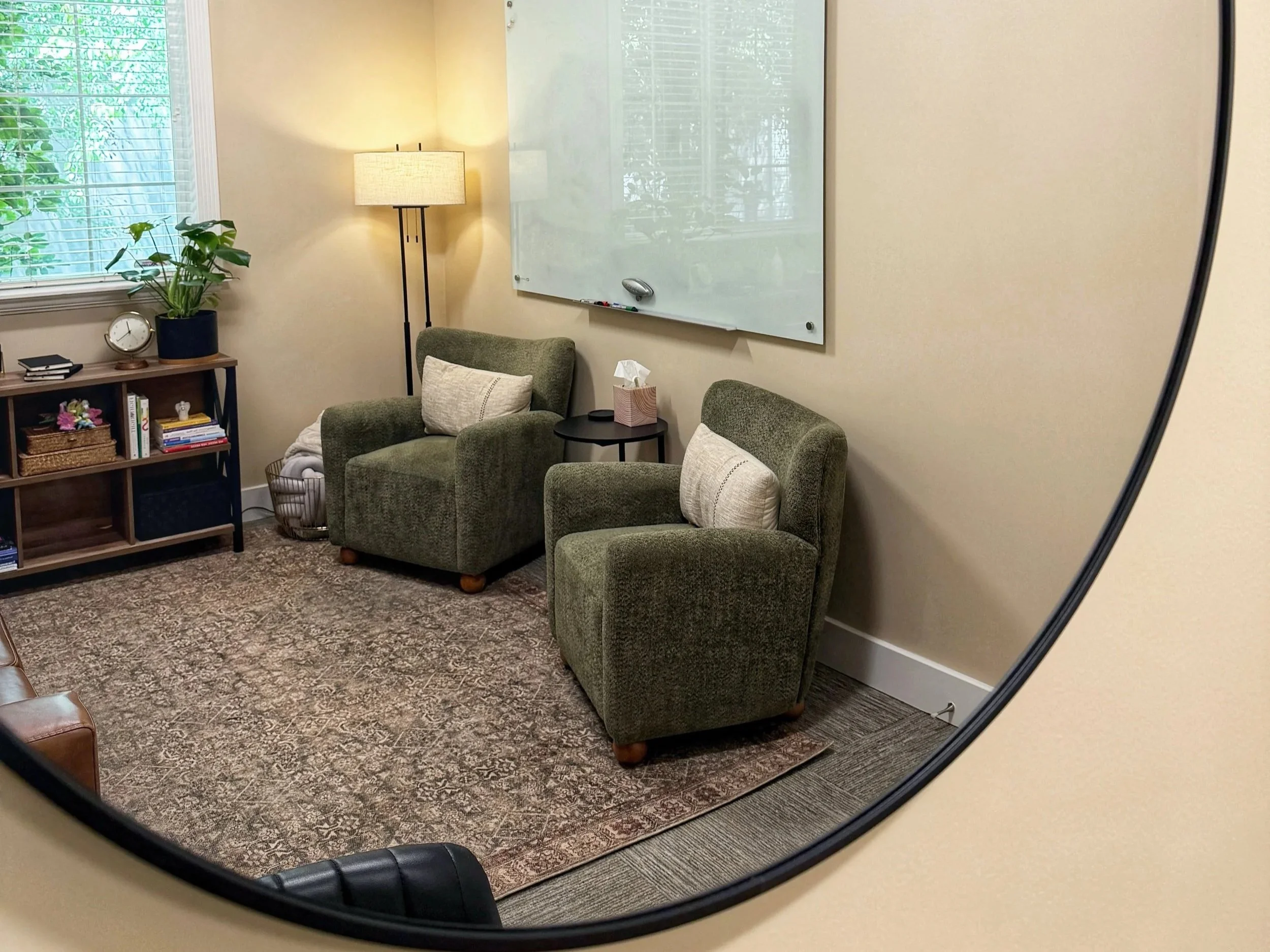 Green armchairs with light-colored pillows beside a whiteboard in the Willow Brook Counseling Center office.
