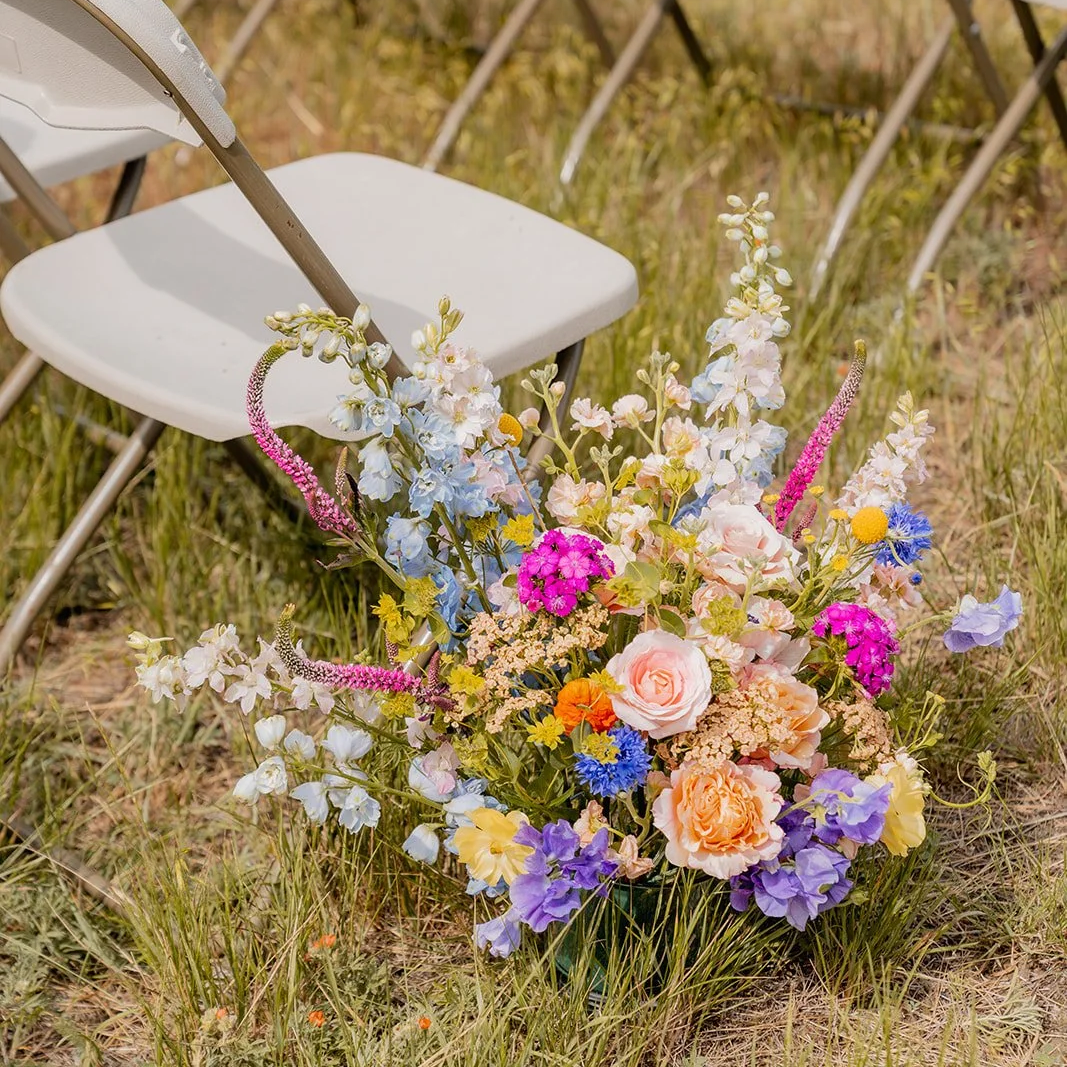 A colorful bouquet of flowers on the grass next to a white chair and other chairs in the background.