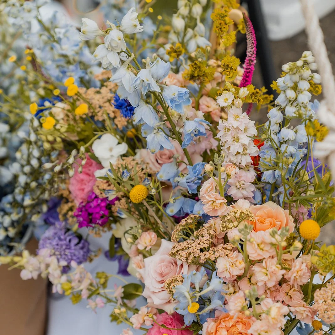 A colorful bouquet of various fresh flowers, including roses, delphiniums, and other vibrant blossoms.