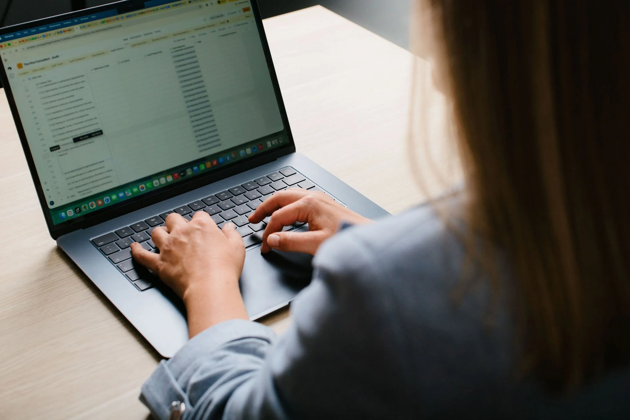 A person typing on a MacBook laptop at a desk, with email and various app icons visible on the screen and dock.