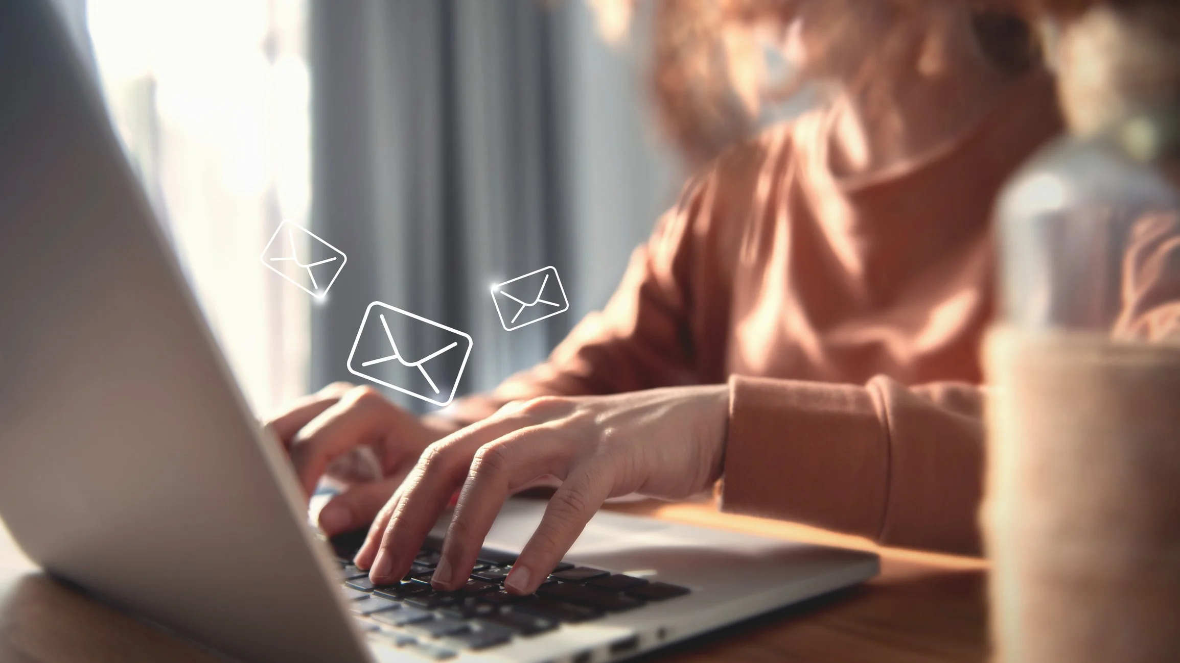 Person typing on a laptop with email icons overlaid in the foreground.