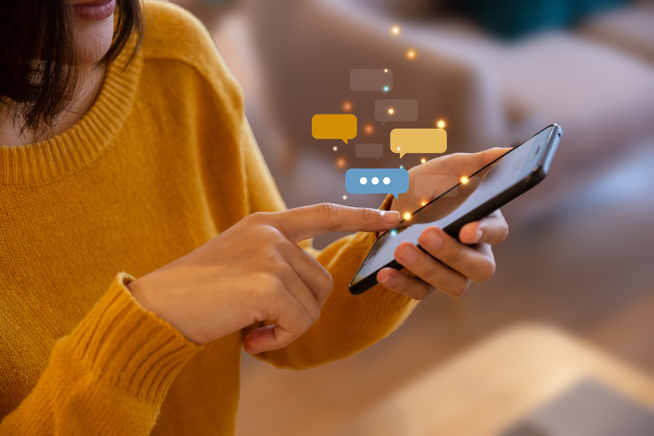 A person in a yellow sweater holding a smartphone with speech bubbles and glowing lights emerging from the screen.