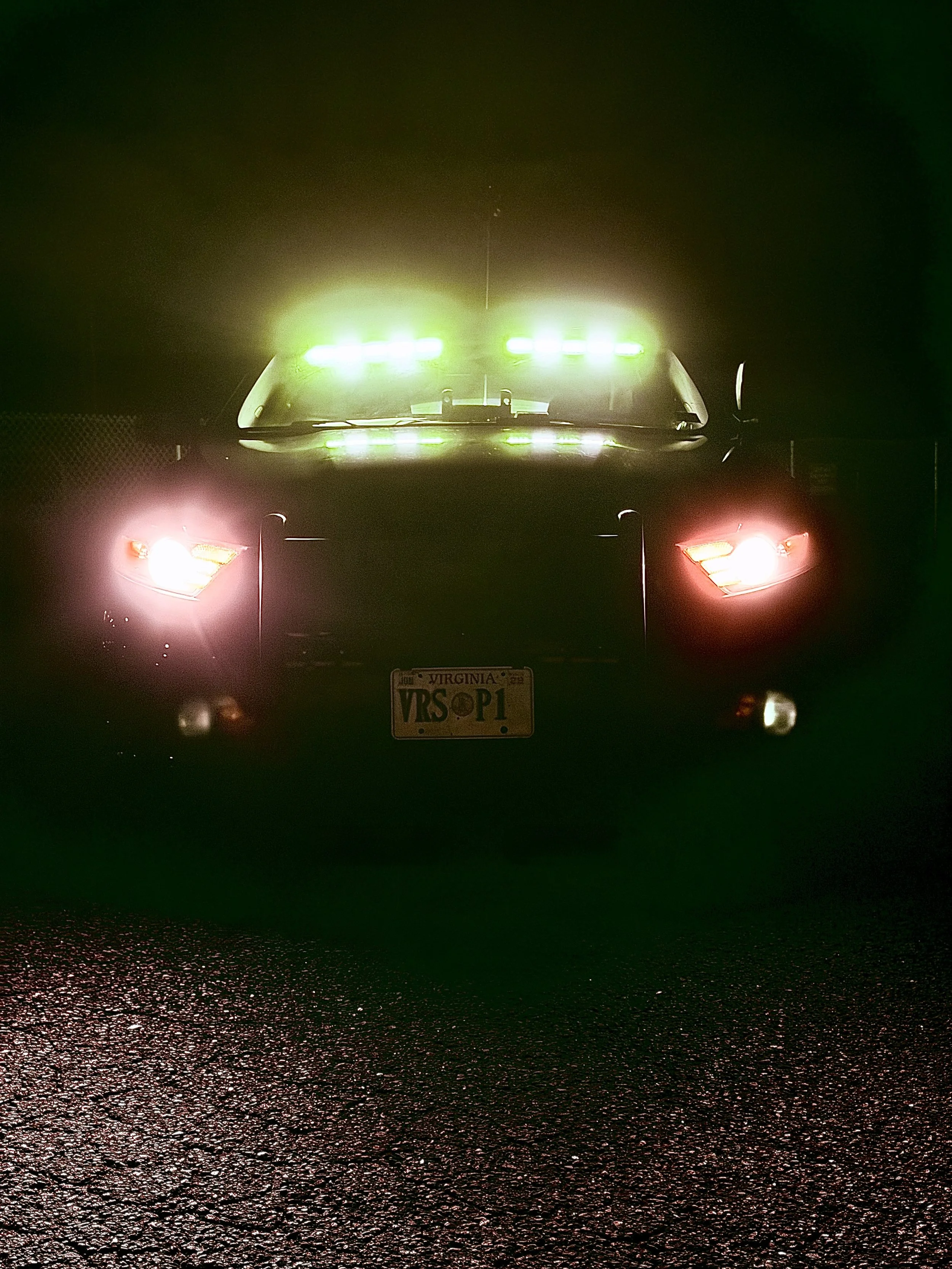 Front view of a police car with green and red flashing lights on a wet road at night.
