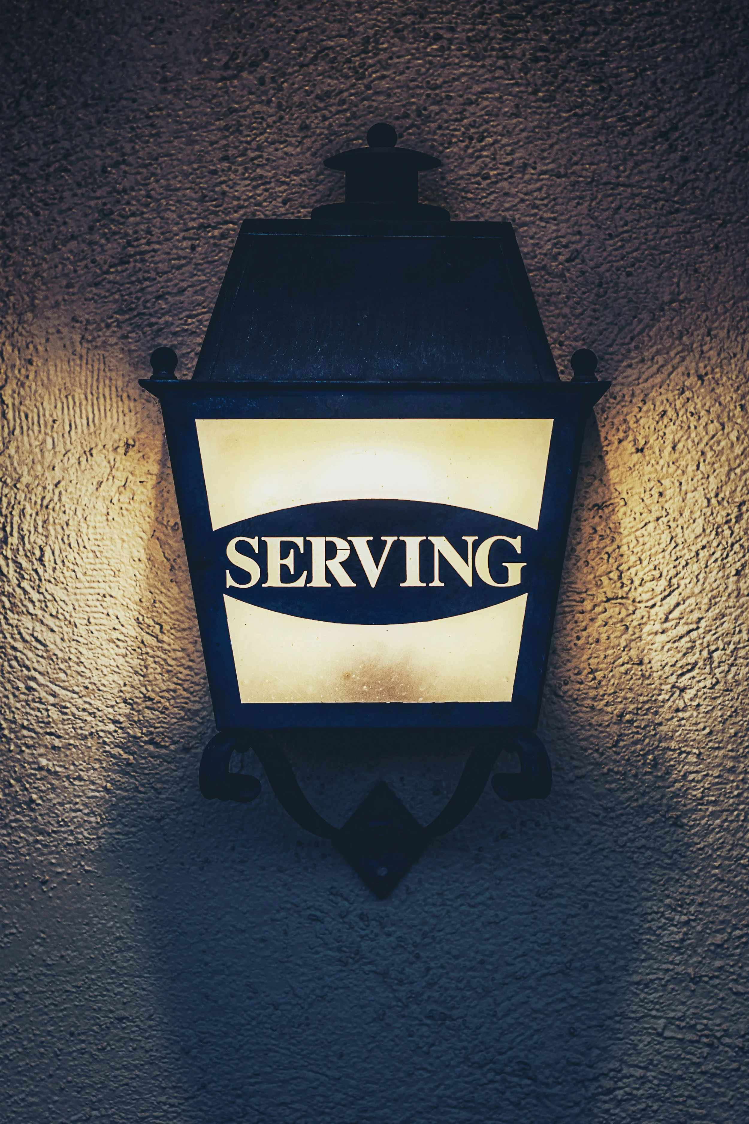 A lit lantern sign reading "Serving," symbolizing a commitment to service