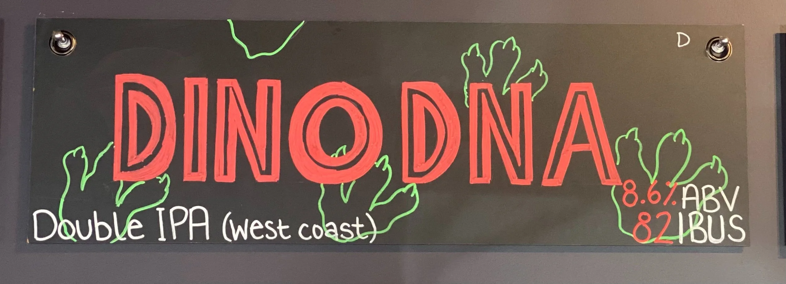 Chalk design that says DINO DNA in red in the middle with dinosaur footprints in green behind. Says double IPA (West Coast) at the bottom.