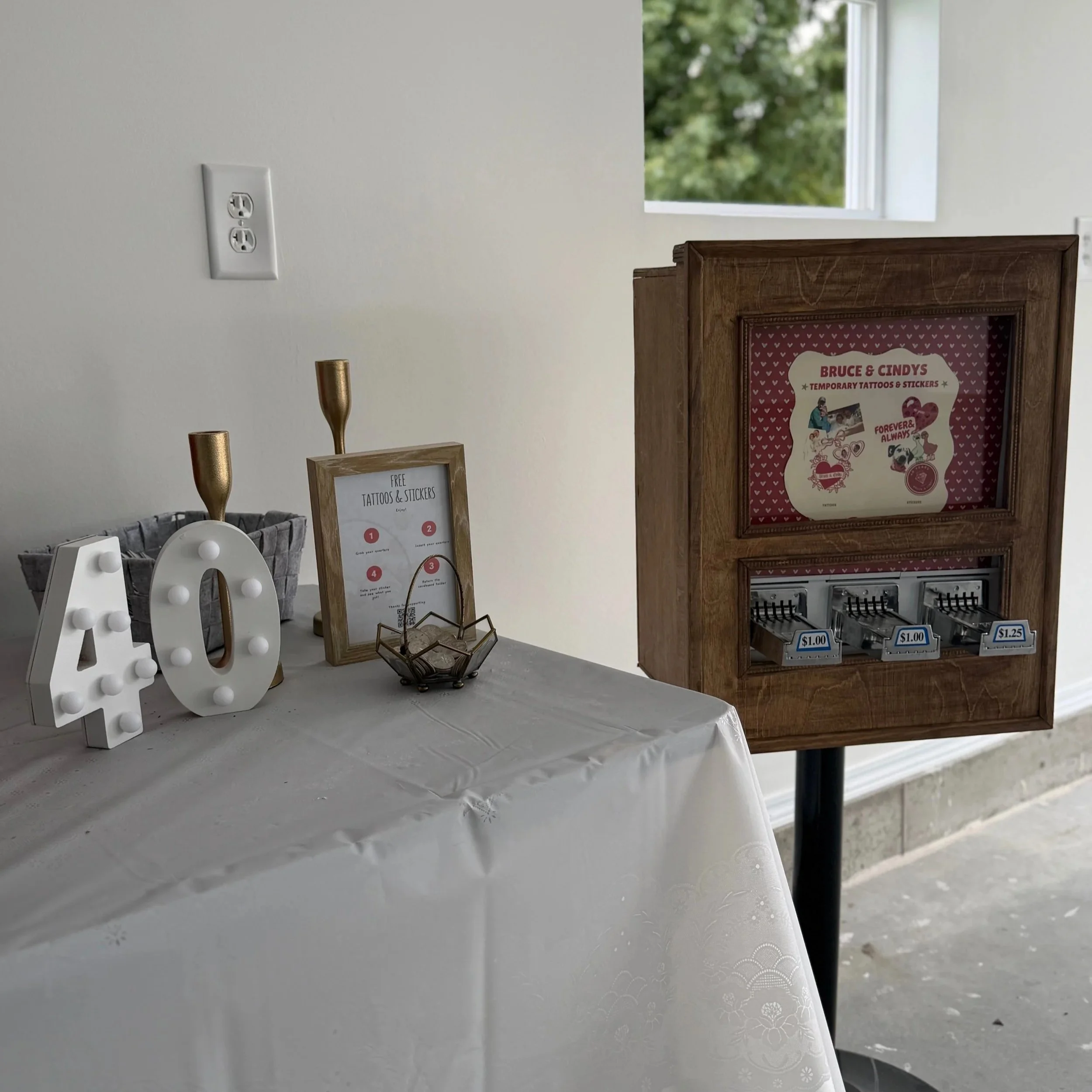 set up for a sticker vending machine. machine is on the right and a table with the decorations and set up is on the left. The table has a white table cloth
