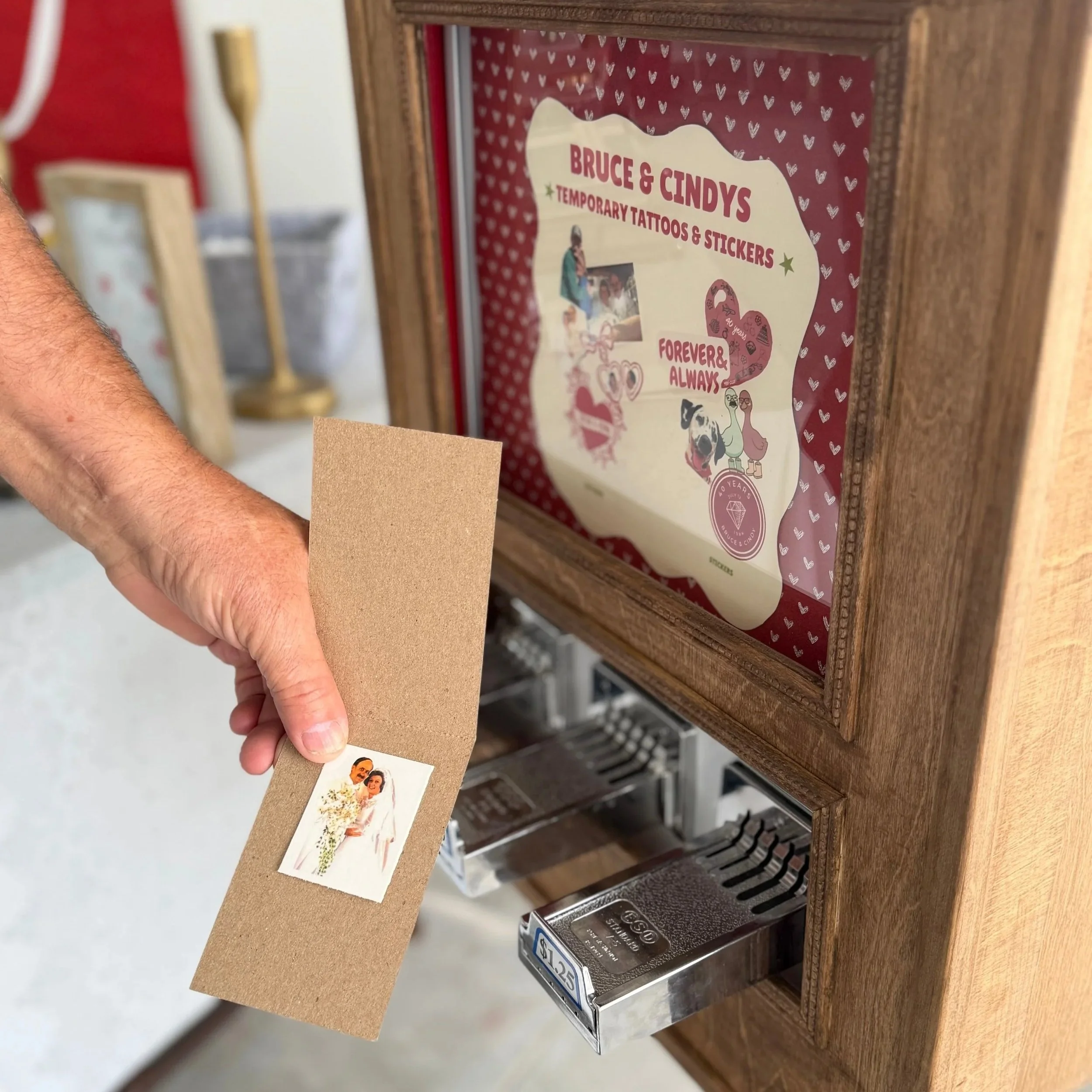 photo of an old sticker vending machine with a mans hand holding the prize he recieved from the machine. its a temporary tattoo of a bride and groom