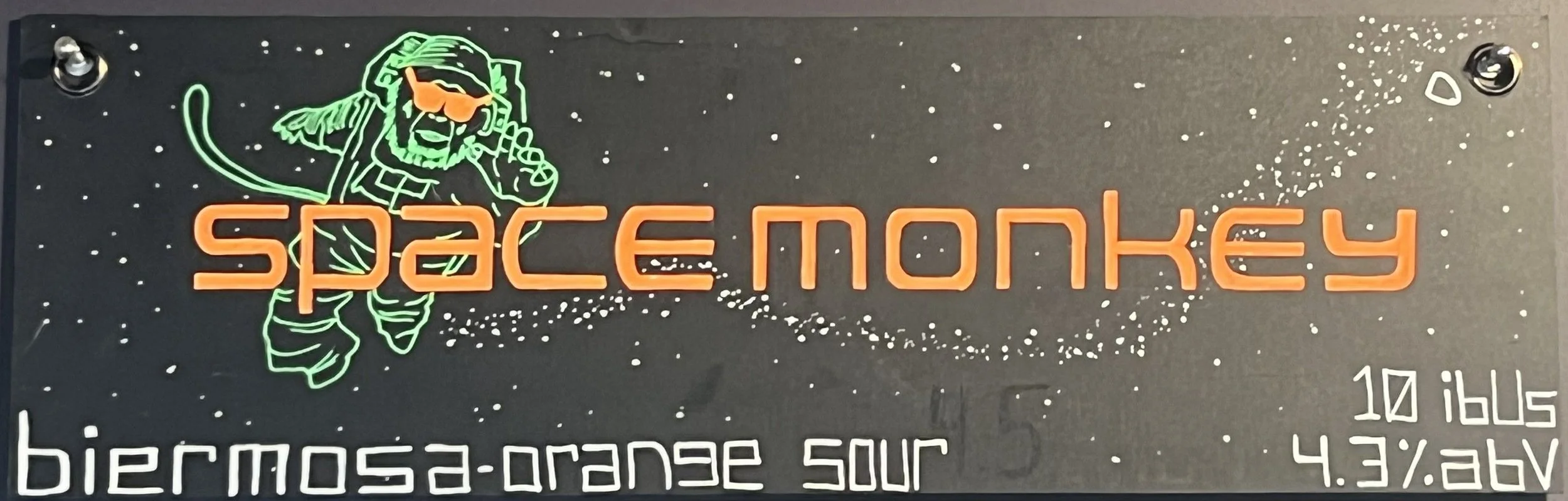 Chalk design that says space monkey in orange with a drawing of a green monkey astronaut with orange sunglasses that says biermosa-orange sour at the bottom.