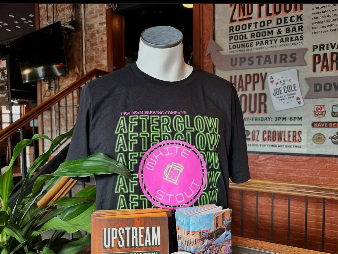 t-shirt on a mannequin in black with neon green words that say afterglow five times with a pink circle in the middle that says white stout with a beer glass drawing in the middle.