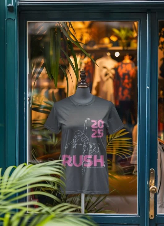 t-shirt on a mannequin in a window. the shirt is grey that says 2025 in the right top corner and RUSH at the bottom both in pink with a stencil drawing of a girl dancing.
