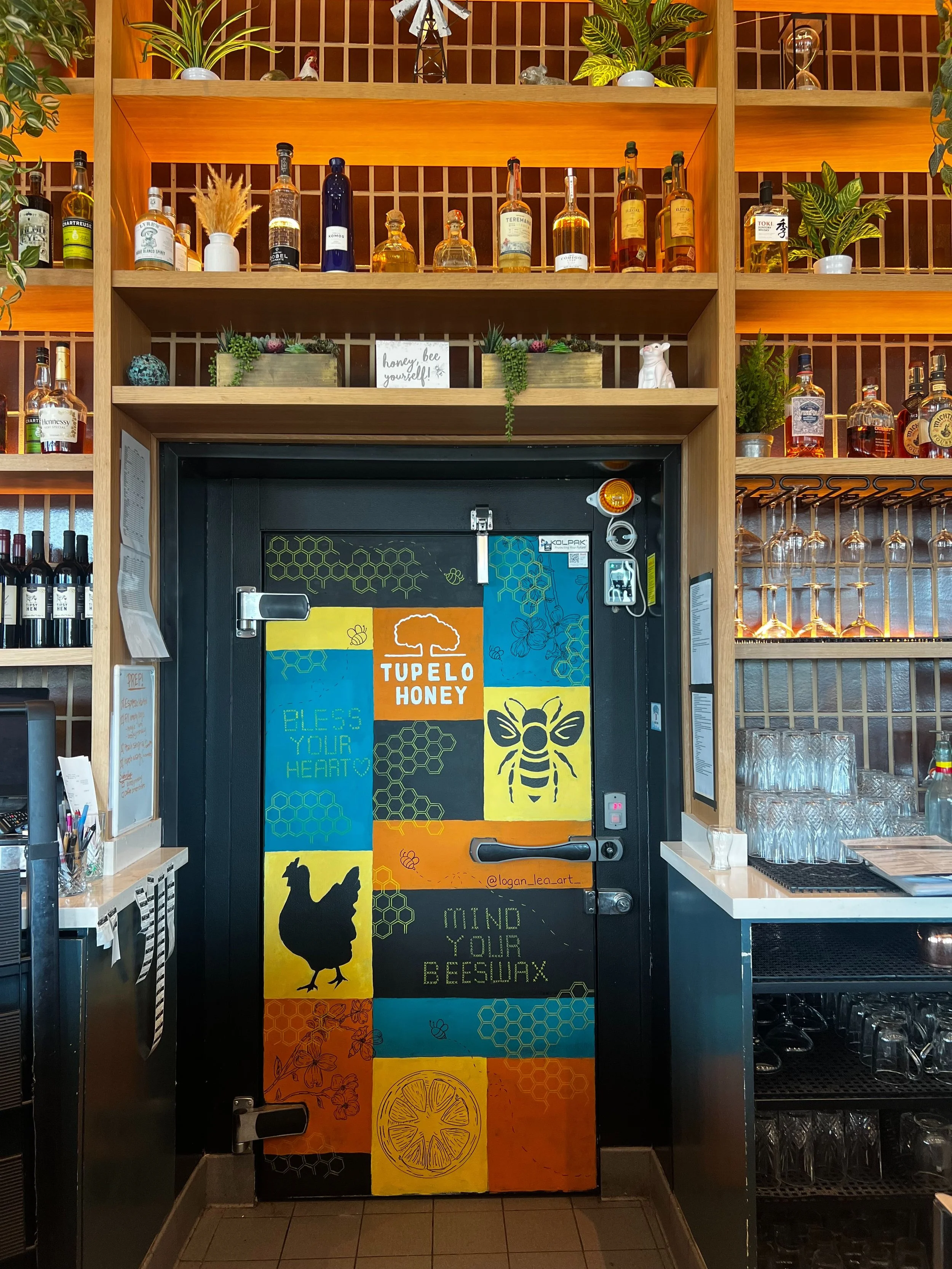 Tupelo Honey mural with orange yellow and blue squares, drawings of honey comb, a chicken, bees, a lemon and flowers. 