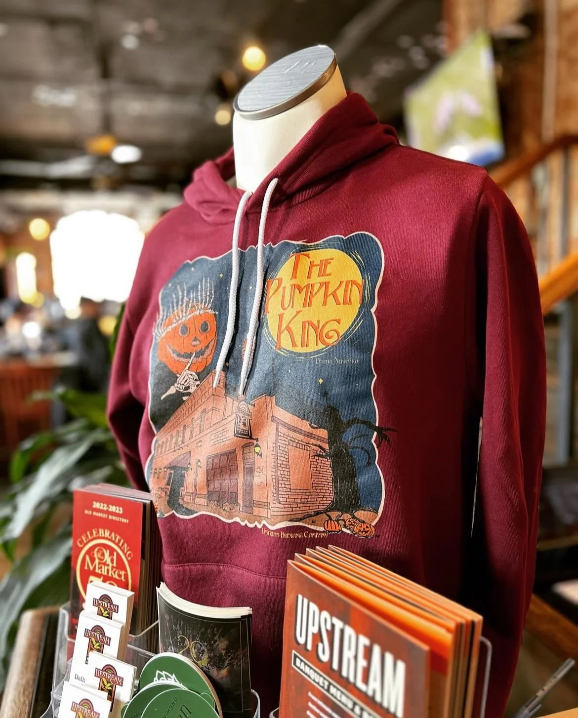 hoodie on a mannequin in cranberry red of an art print of a pumpkin king man above a building in the dark. very spooky vibes. with a  yellow moon in the corner that says The Pumpkin King