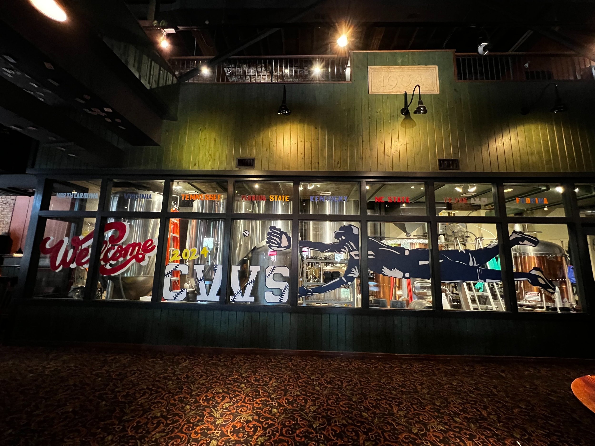 window art across 8 windows that says welcome 2024 cws with a silhouette painting of a baseball player catching a baseball
