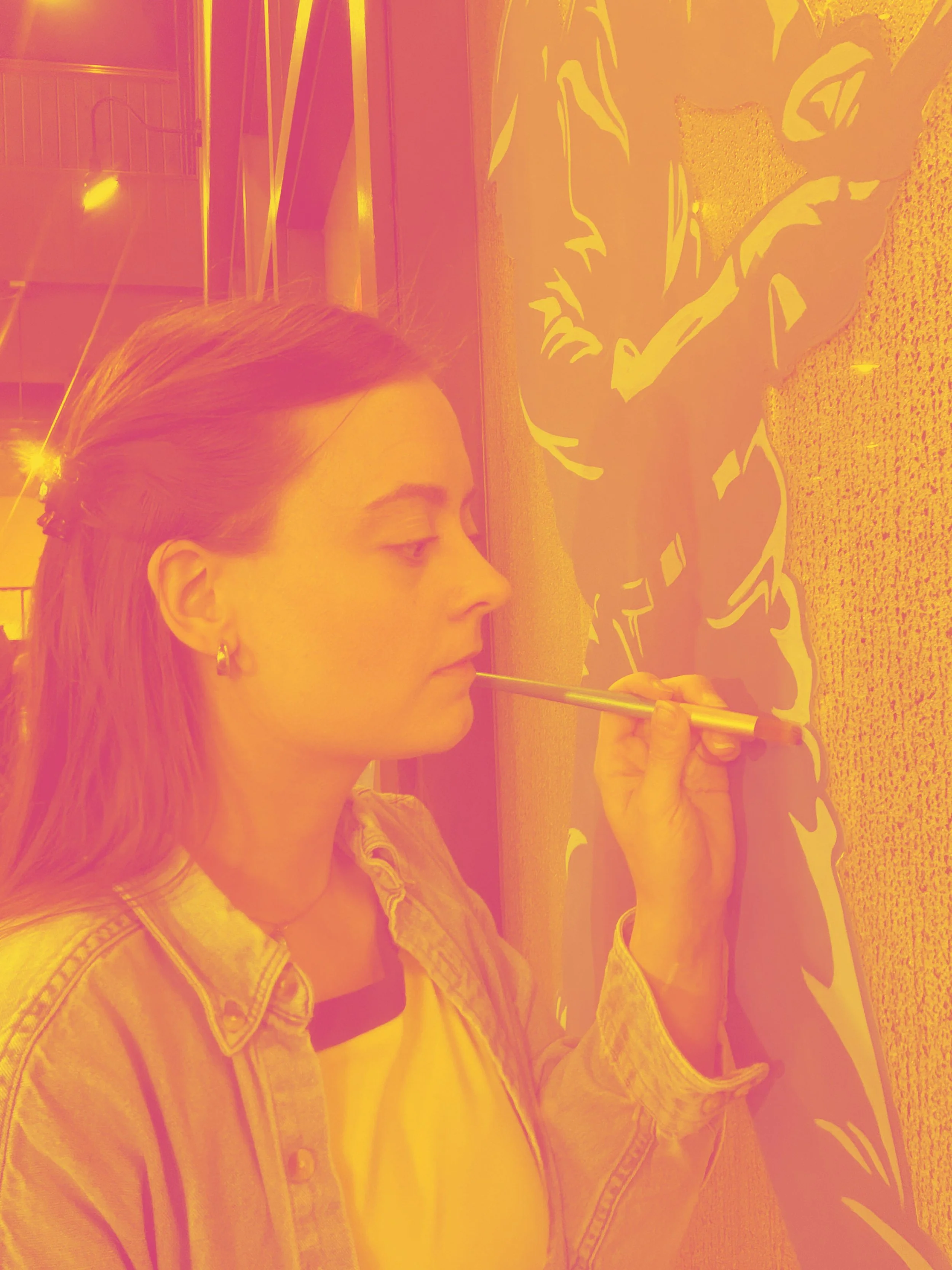 photo of a woman painting on a window in a pink and yellow hue