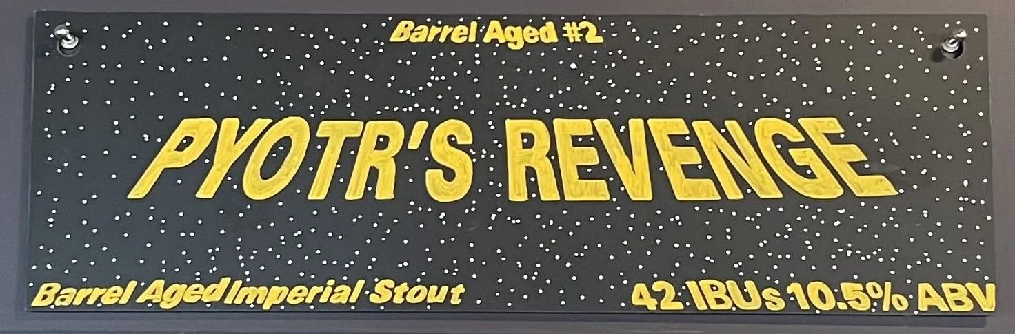 Star Wars-inspired chalk drawing that says Pyotr's Revenge. Like the opening credits of a Star Wars movie, with space stars behind it. Words in yellow. says barrel aged #2 at the top and barrel-aged imperial stout at the bottom.