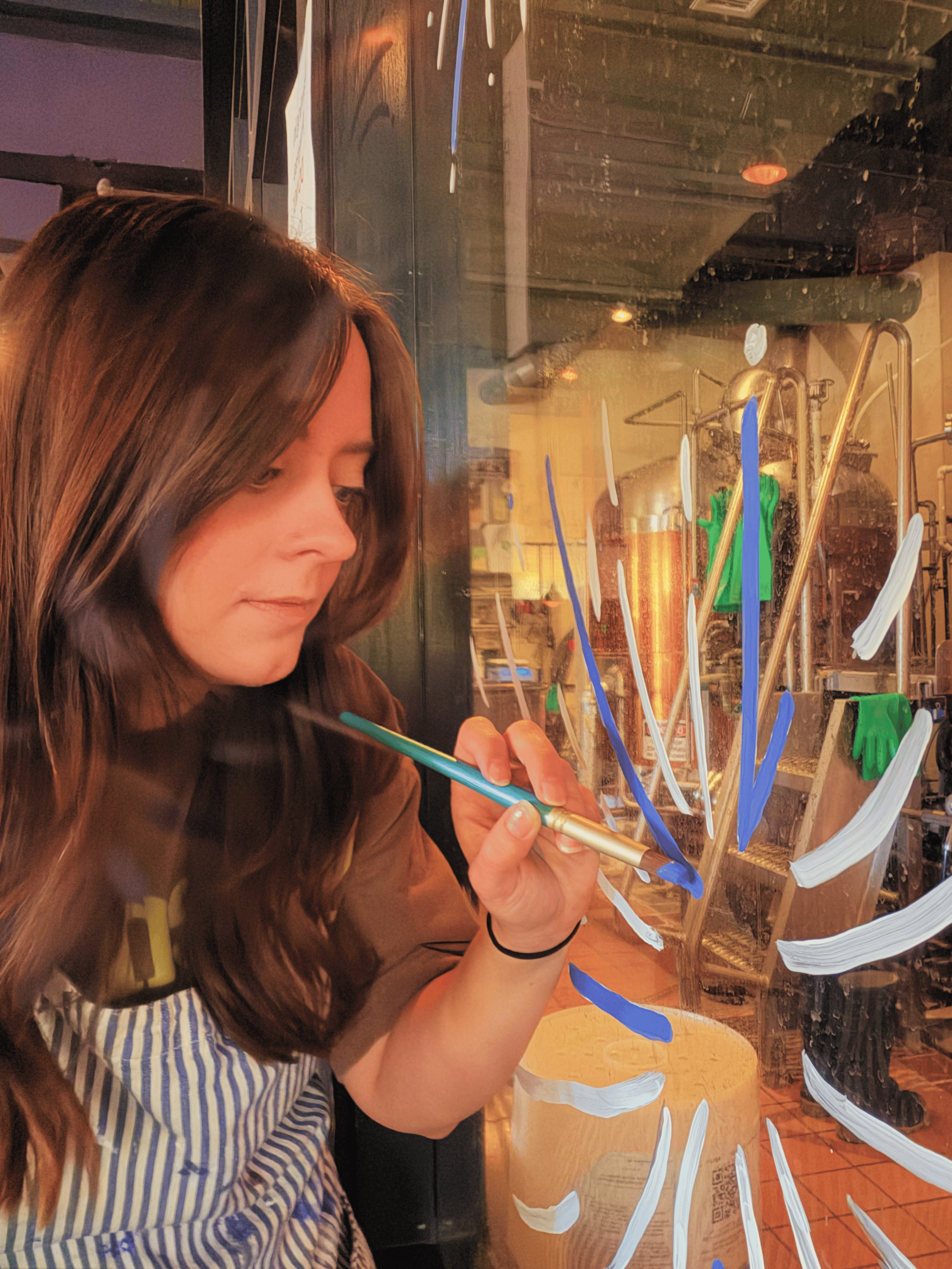 woman with brown long hair painting on a window a white and blue firework