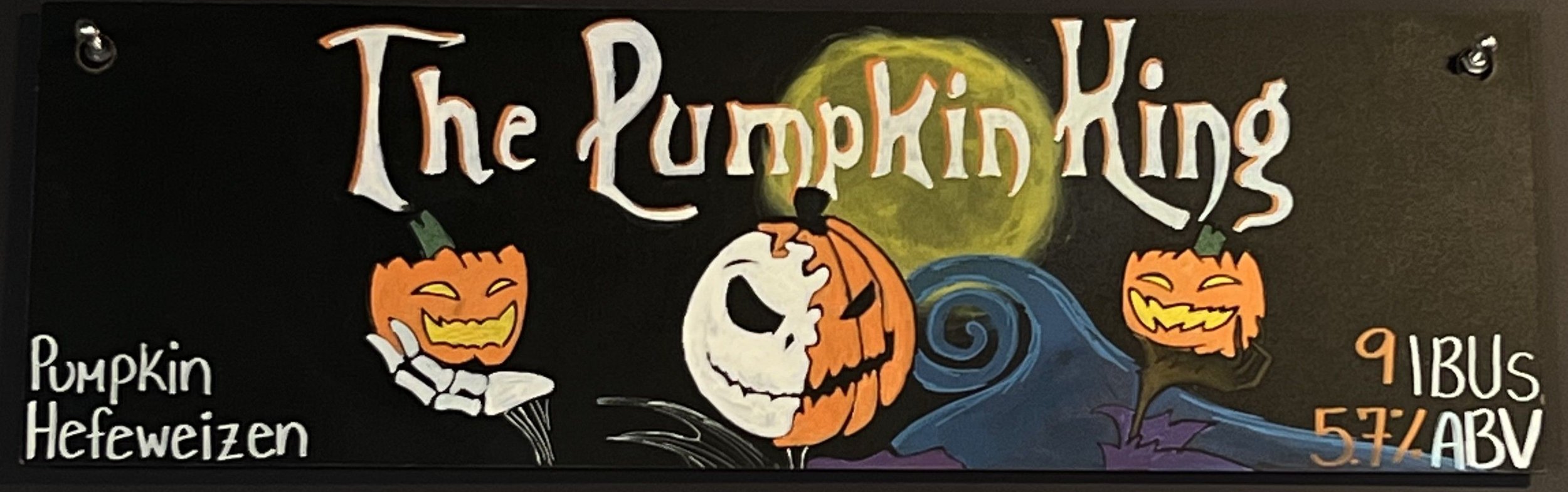 Chalk design of the pumpkin king. Jack Skellington is half Jack, half Pumpkin King. Holding a pumpkin head in each hand with the blue swirl hill behind him, says pumpkin hefeweizen on the left.