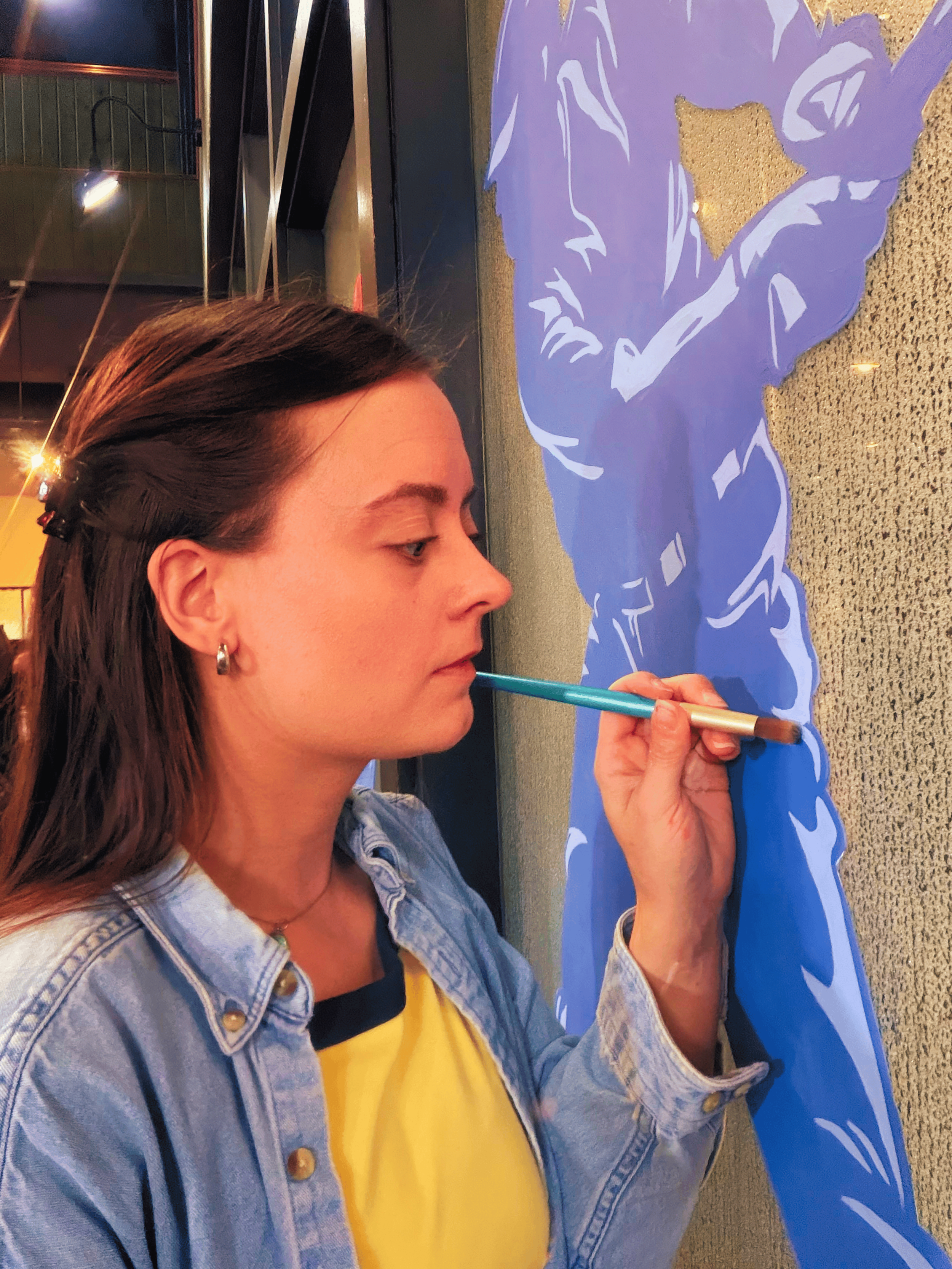 woman with brown hair painting on a window a blue image of a baseball player