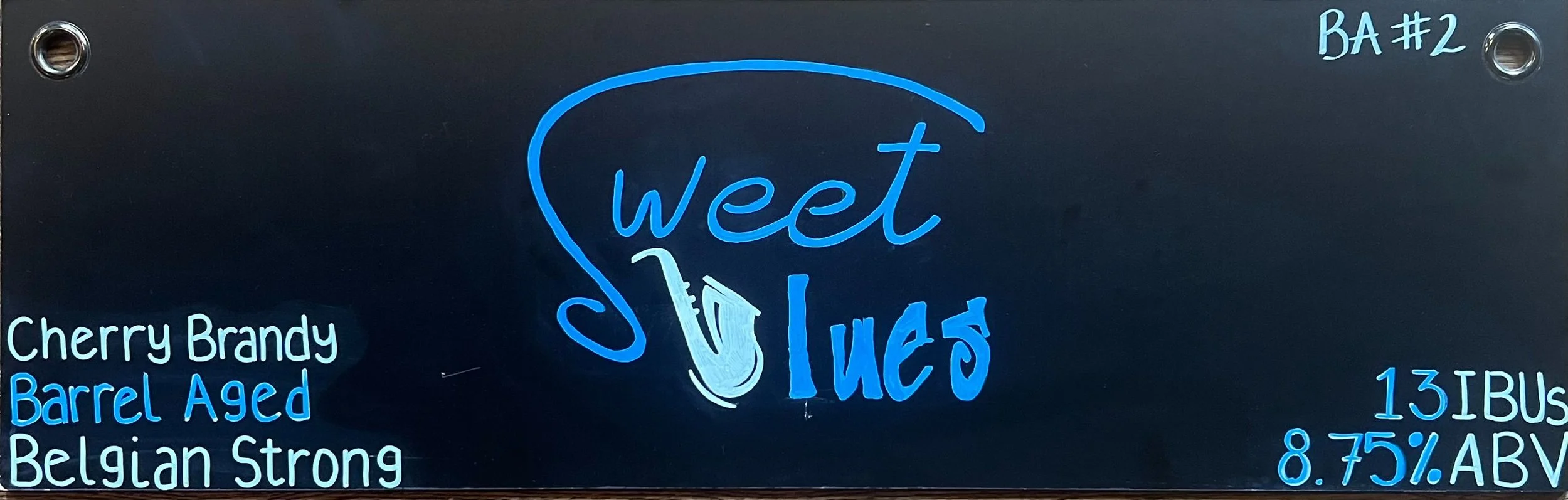 Chalk design that says Sweet Blues in blue color. The B in blues is a saxophone. The s in Sweet swishes all above the word sweet. On the left says cherry brandy barrelaged Belgian strong.