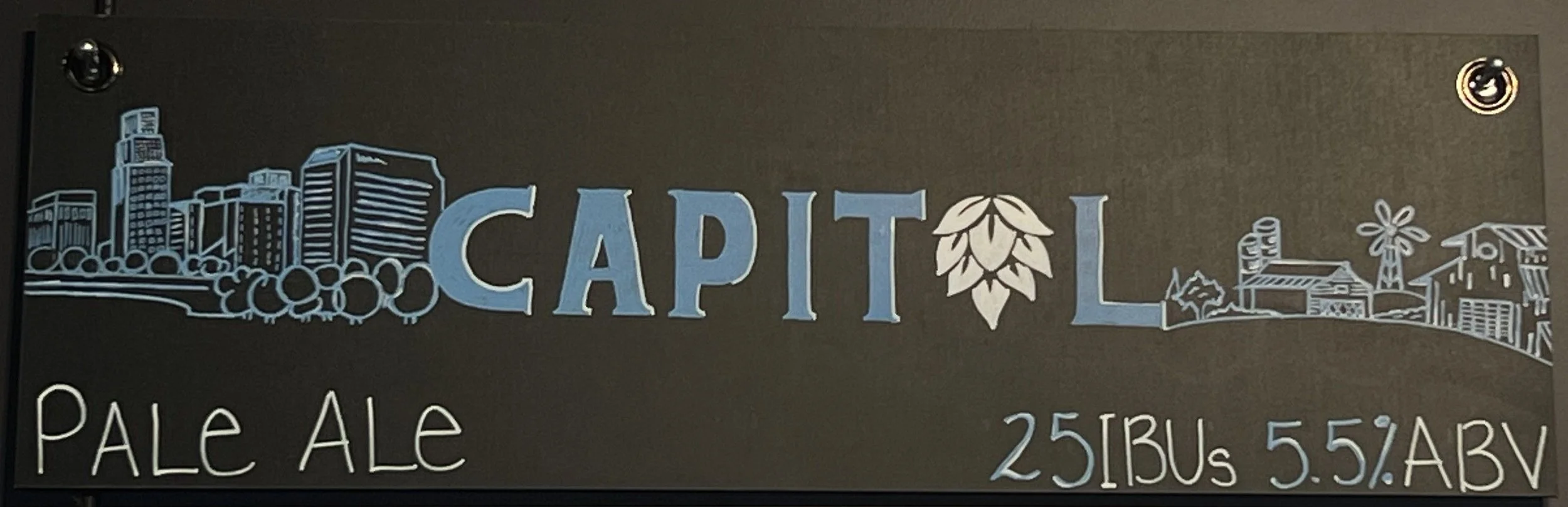 Chalk design in blue and white that says CAPITOL. The O in capital is a drawing of a hop plant. To the left is an outline sketch of Omaha, and to the right of the Capitol is a sketch outline of a farm. Below says pale ale.