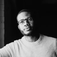 Portrait of a young man with glasses, wearing a light-colored sweatshirt, looking at the camera, black and white photography.