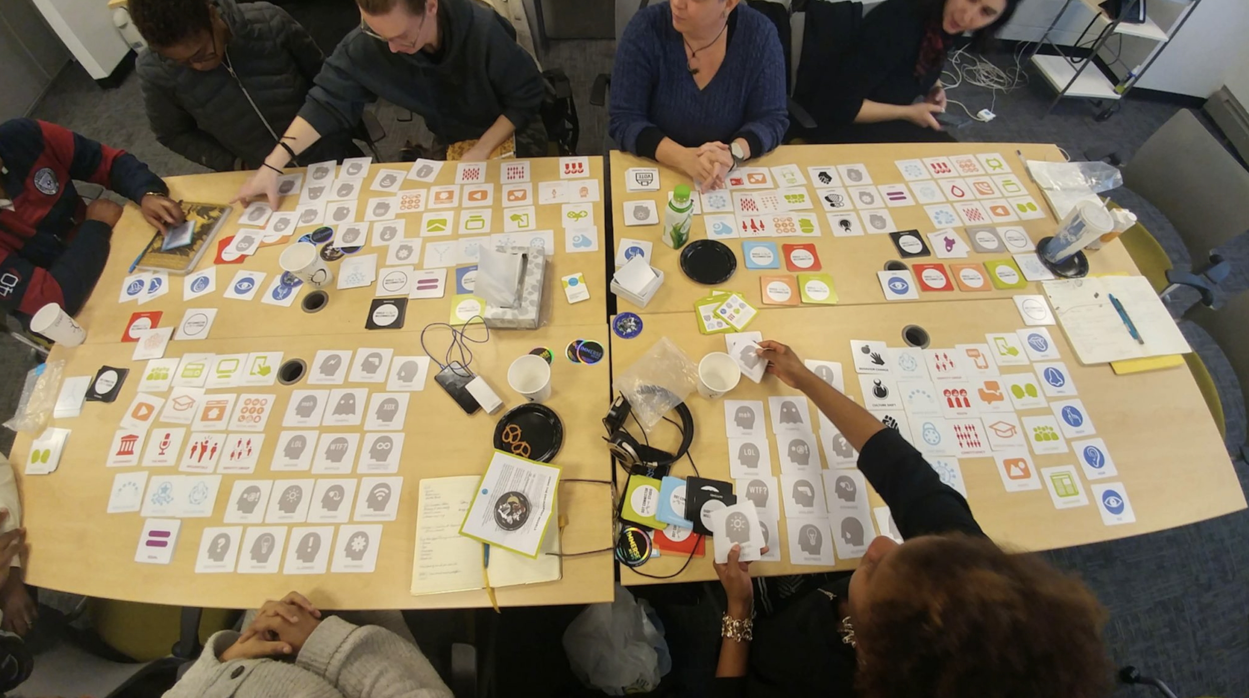 A group of people sitting around a large table playing a card game with colorful cards featuring icons and symbols.