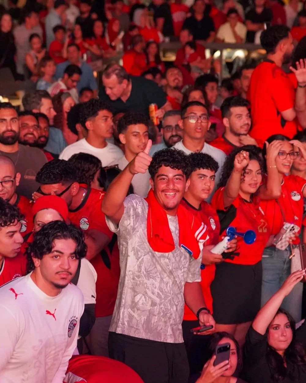 A group of cheering sports fans, many wearing red jerseys, at a stadium.