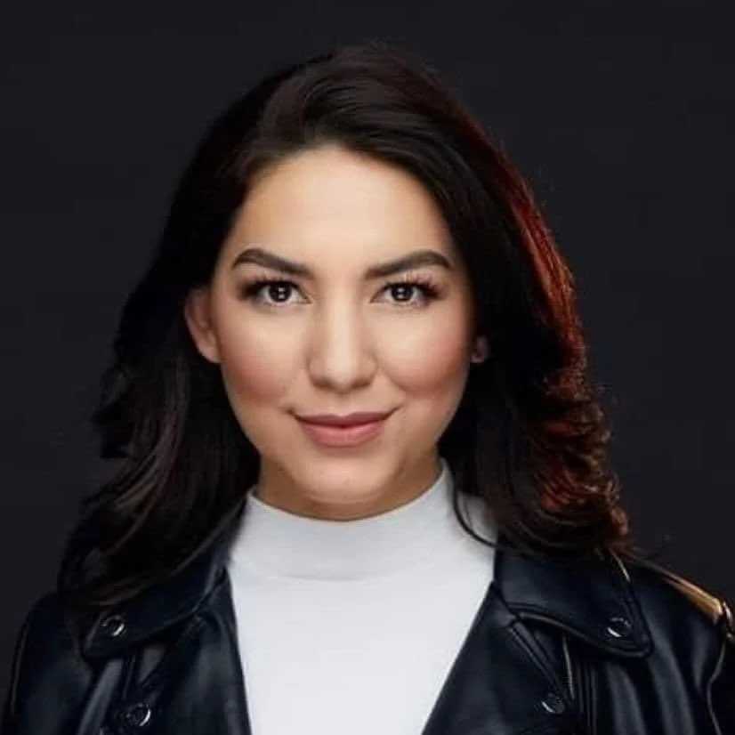 Portrait of a woman with dark hair wearing a leather jacket and a white top against a black background.