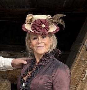 A woman wearing vintage clothing and a decorative hat with feathers, smiling.
