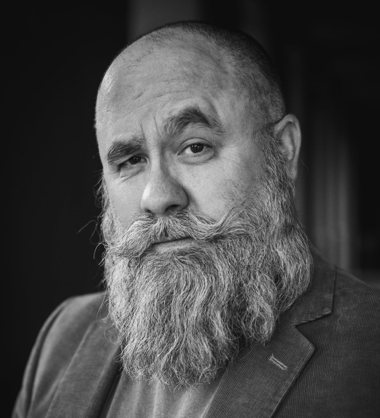 Black and white portrait of a bearded man with a serious expression, wearing a blazer.
